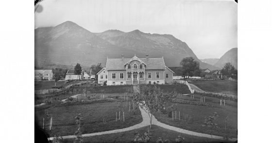 Gammalt svart/kvittbilde av eit staseleg hus i sveitserstil med prydhage framfor fjell på Sunnmøre